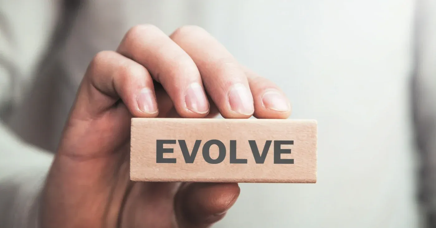 hand holding up a block with the word evolve on it