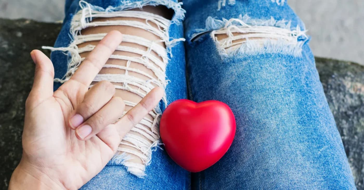 heart in lap of woman wearing ripped jeans