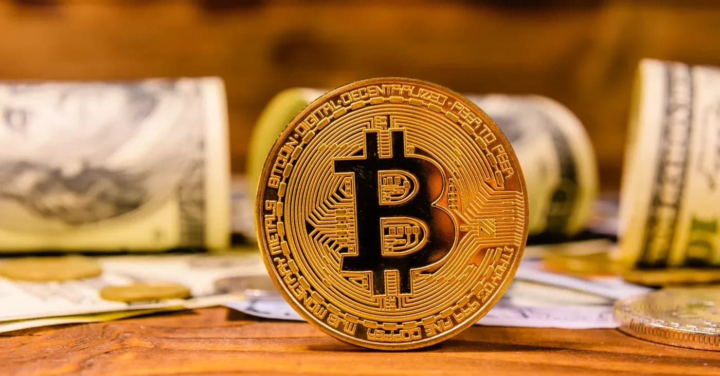 gold coin with bitcoin symbol in front of paper money rolls