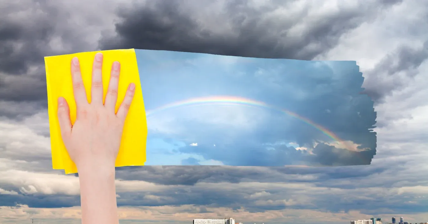 hand and cloth wiping away cloudy sky to reveal rainbow