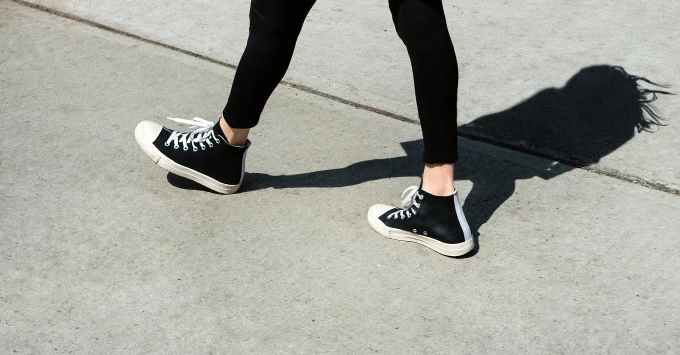 person walking in sneakers with shadow on sidewalk