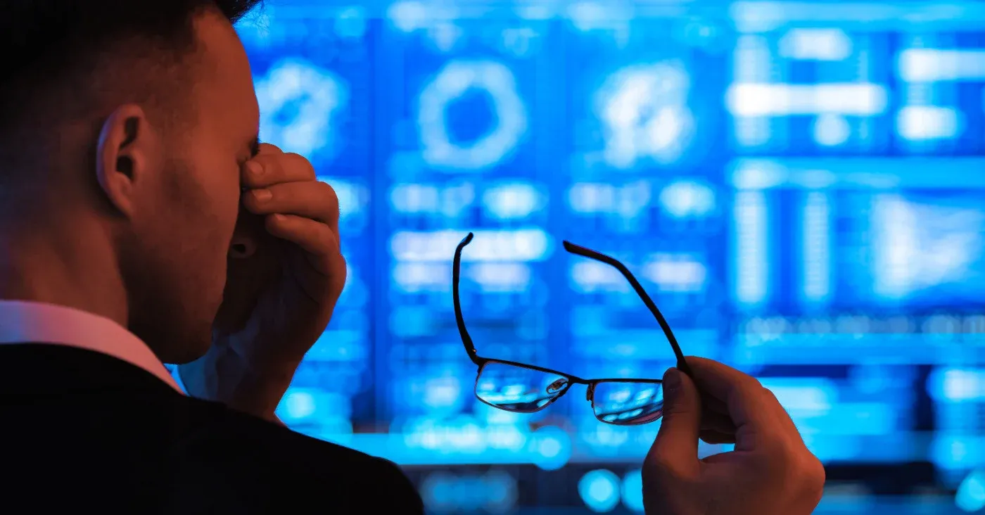 fatigued man rubbing eyes at monitors
