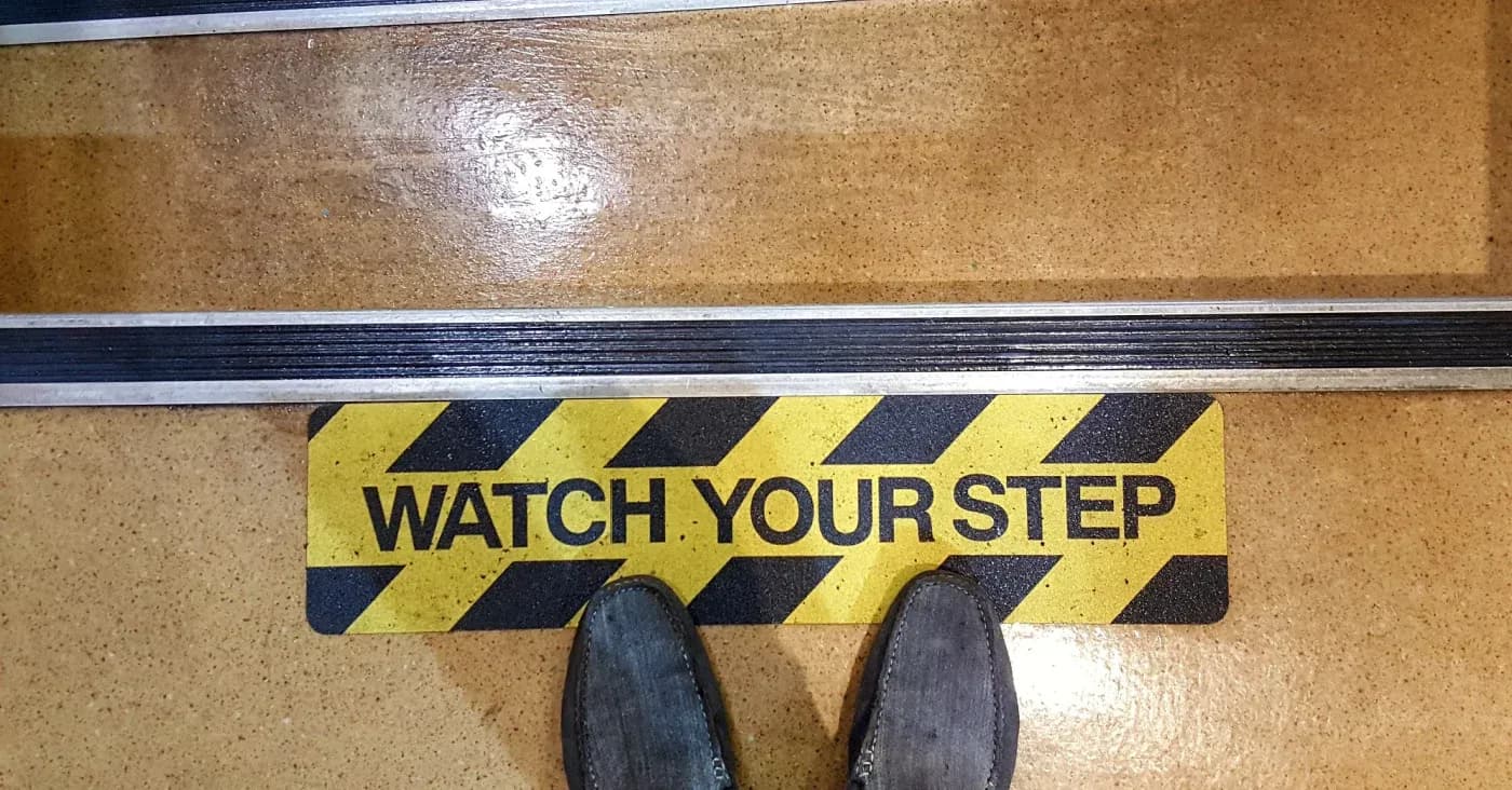 feet standing on watch your step warning on stairs