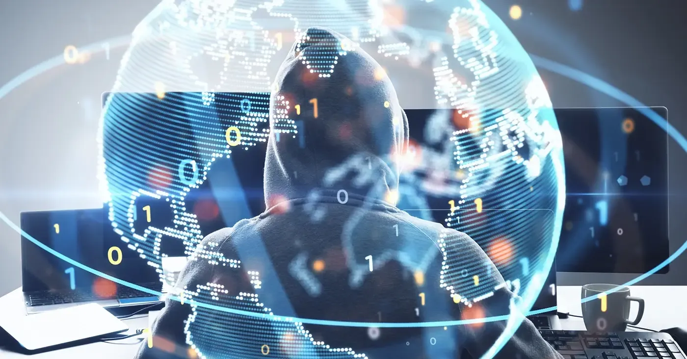 hooded figure at computer with globe hologram